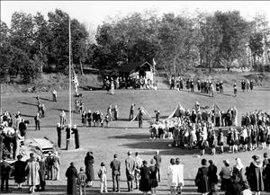 Crowds of people scattered across a field, a flagpole, and large banners. Trees in the background. 